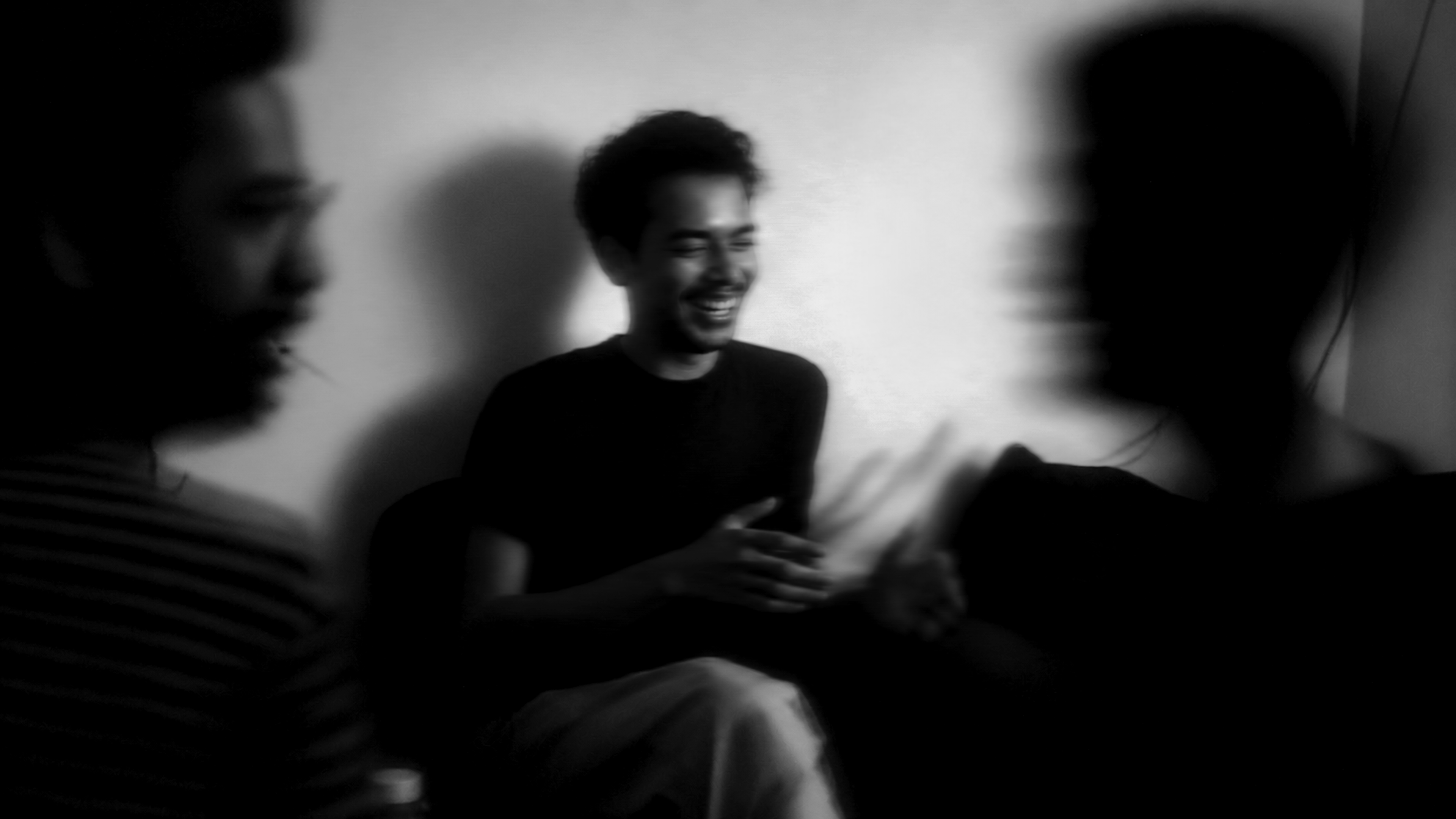 Three anonymous creators sharing a candid, softly blurred laugh in neutral black and white.